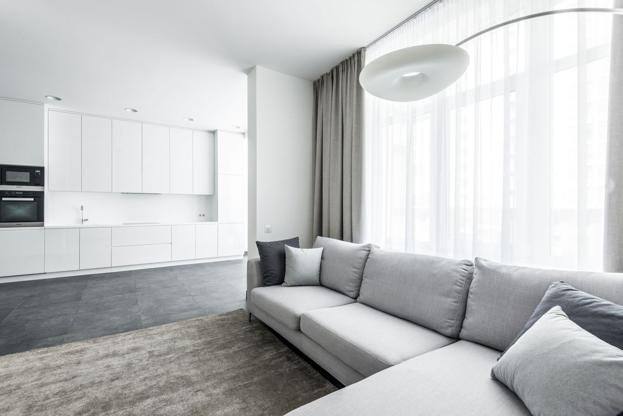 Salon lumineux et contemporain avec un canapé confortable et une cuisine au fond au style minimaliste.